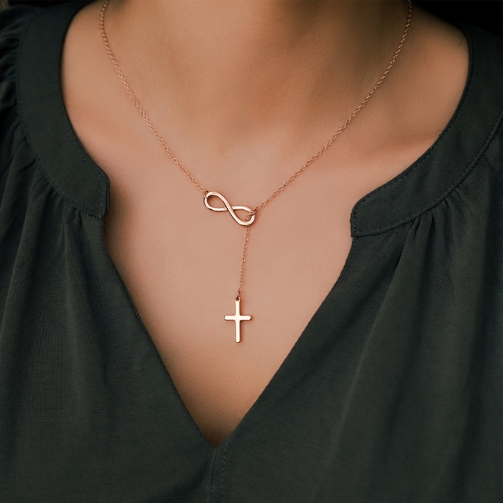 Rose gold necklace with infinity and cross pendants on a person wearing a black top.