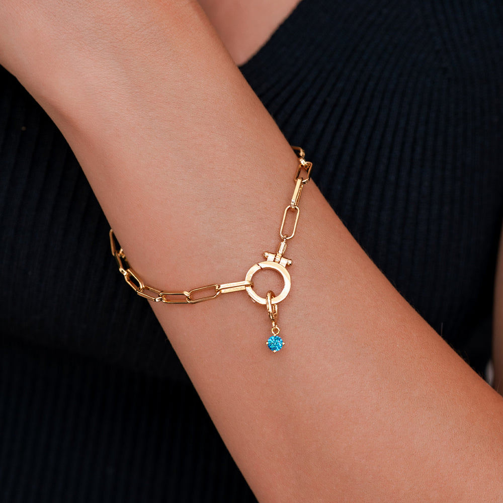 Gold bracelet with a blue gemstone on a wrist against a black background
