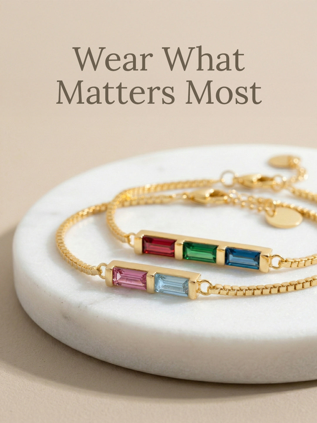 Gold bracelets with colorful gemstones on a marble surface with 'Wear What Matters Most' text.