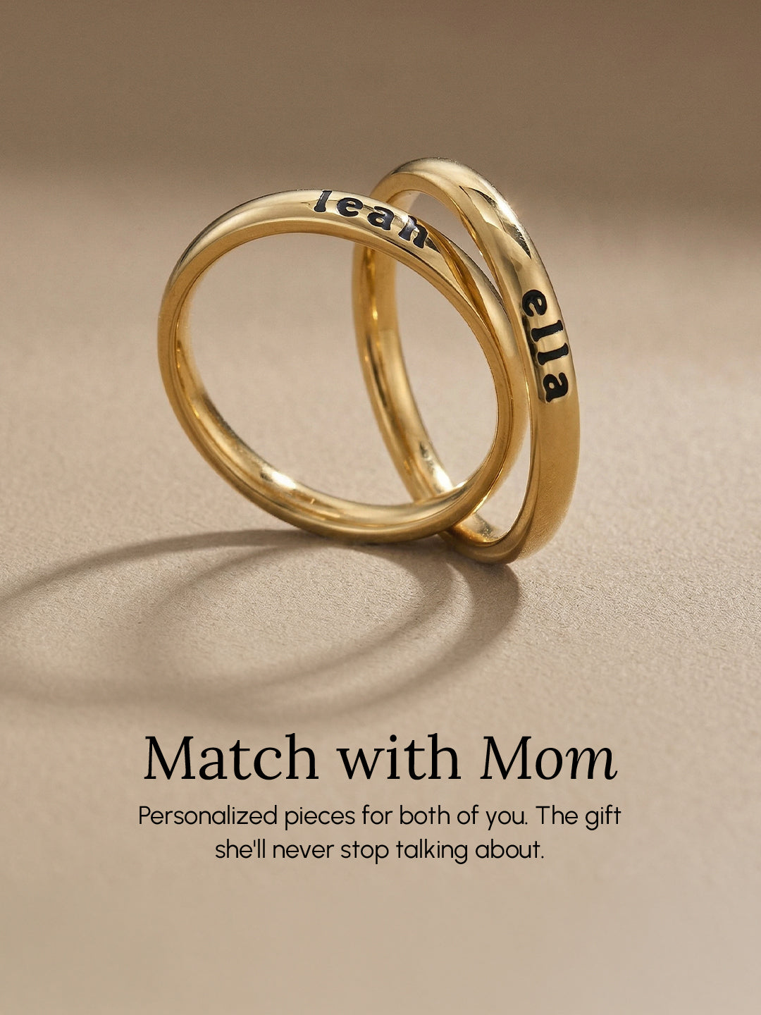 Two gold rings engraved with names overlap on a beige background above the text: “Match with Mom. Personalized pieces for both of you. The gift she’ll never stop talking about.