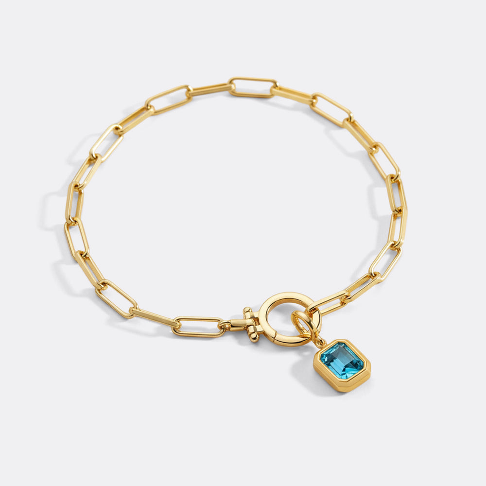 Gold bracelet with a blue gemstone charm on a white background