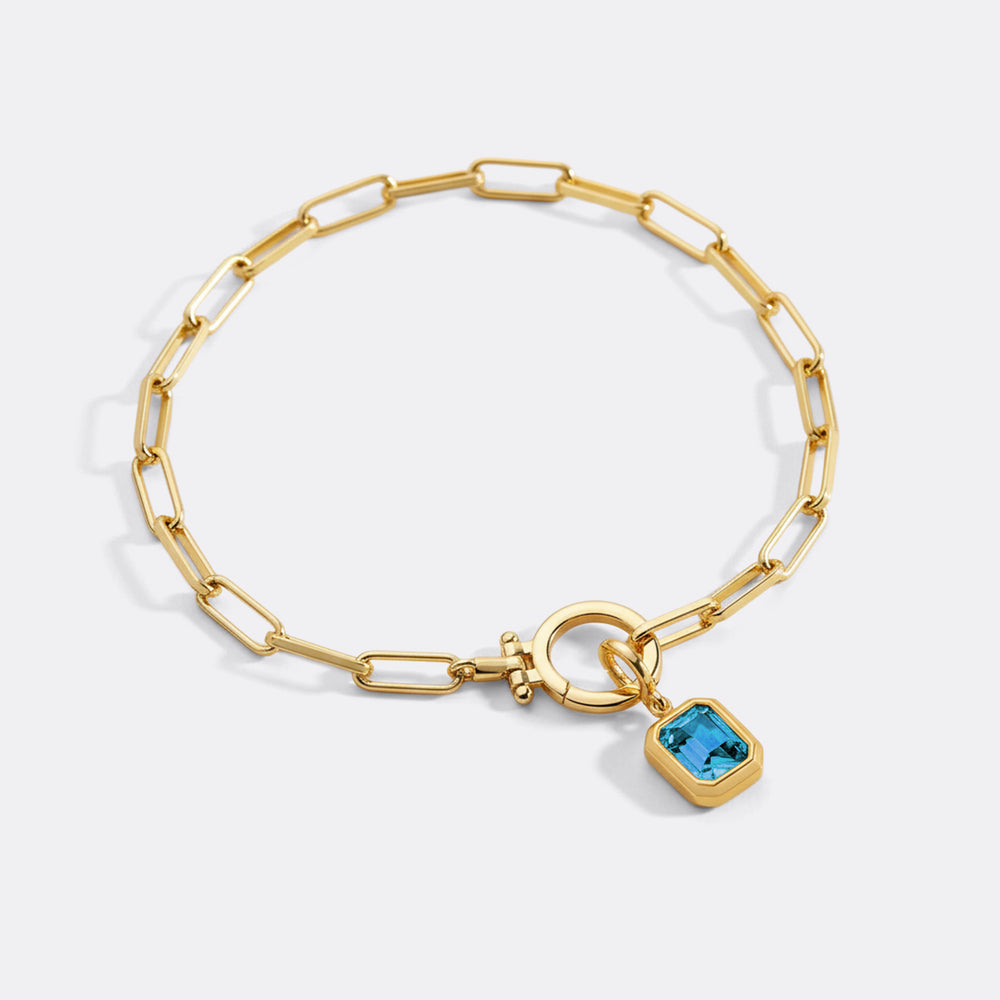 Gold bracelet with a blue gemstone charm on a white background