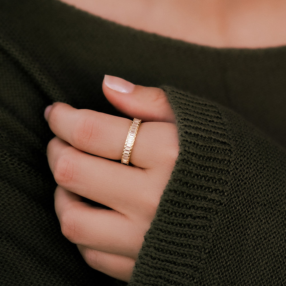 Hand in a dark green knit sweater wearing a gold eternity band set with clear baguette-cut stones.