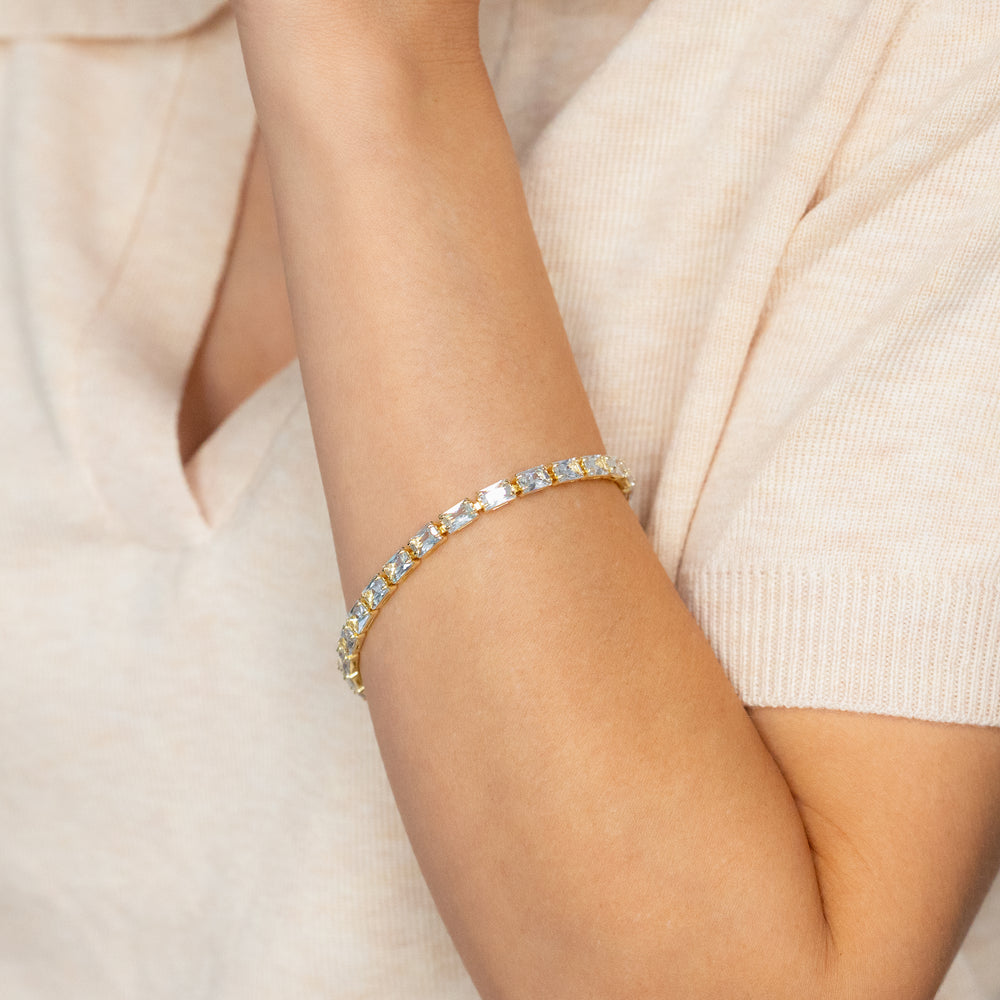 Gold bracelet with clear stones on a person's wrist against a neutral background