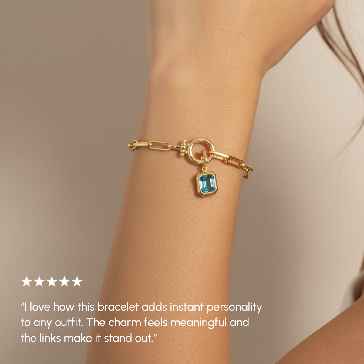 Gold bracelet with a blue gemstone charm on a wrist, with a neutral background.