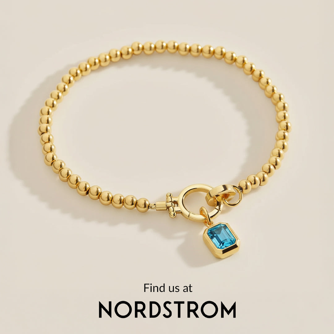 Gold bracelet with a blue gemstone charm on a beige background, featuring Nordstrom branding.