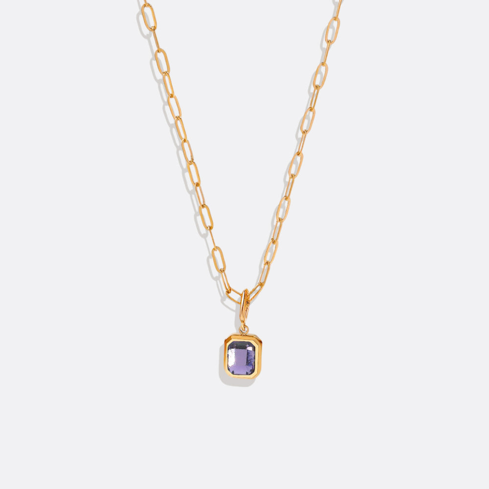 A gold-colored necklace with a baguette-cut birthstone pendant suspended from a paperclip chain.
