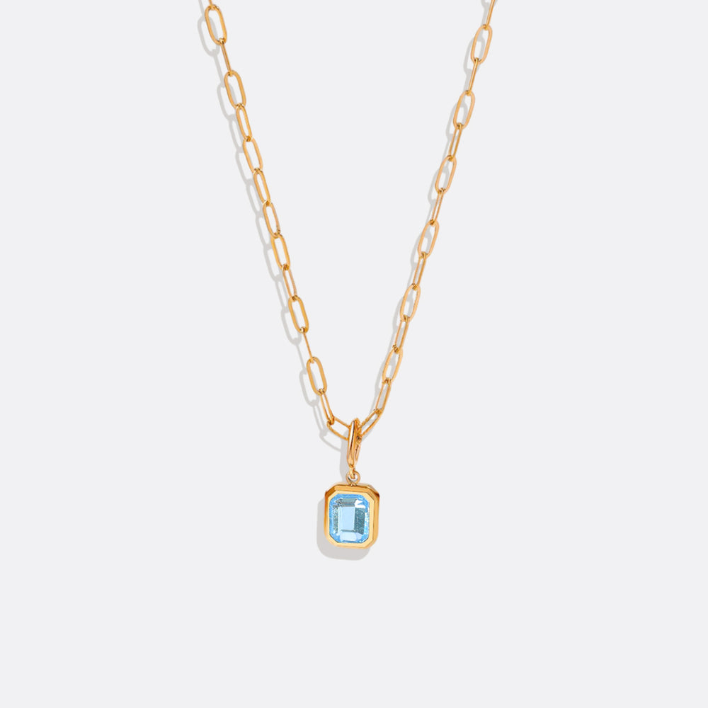 A gold-colored necklace with a baguette-cut birthstone pendant suspended from a paperclip chain.