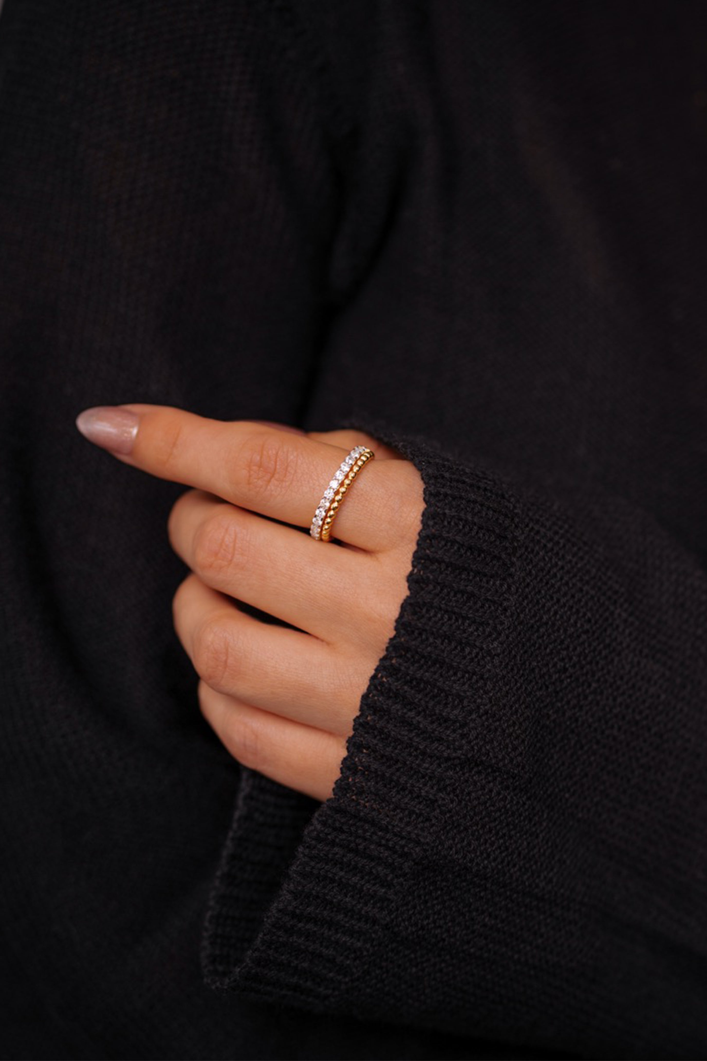 Hand wearing a gold ring with a black sweater background