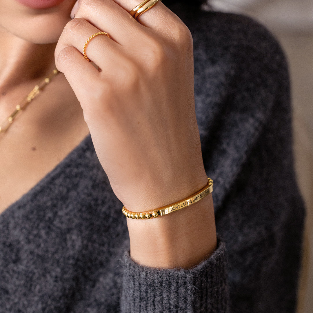 Close-up of a person wearing gold bracelets and rings on a blurred background