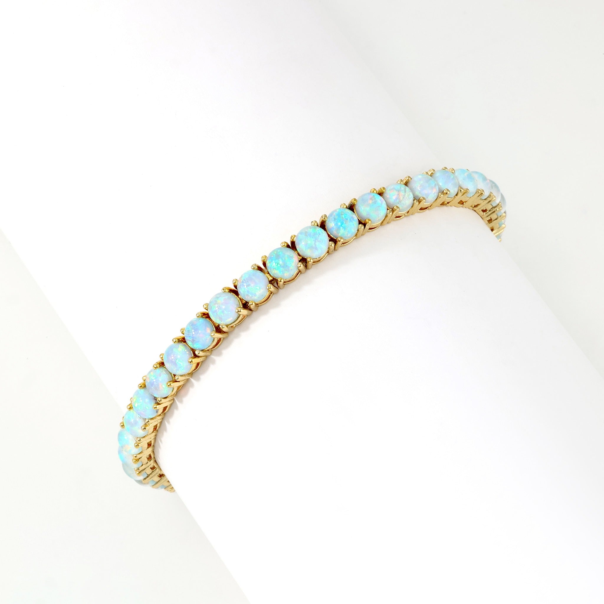 Gold blue opal tennis bracelet wrapped around a white display form on a light background.