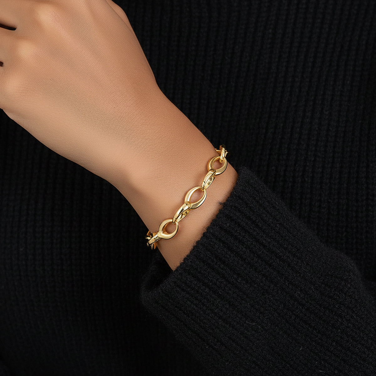 Gold chain bracelet on a wrist against a black background