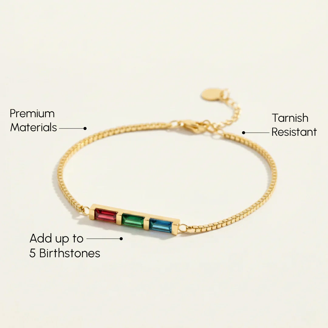 Gold bracelet with embedded birthstones on a light beige background