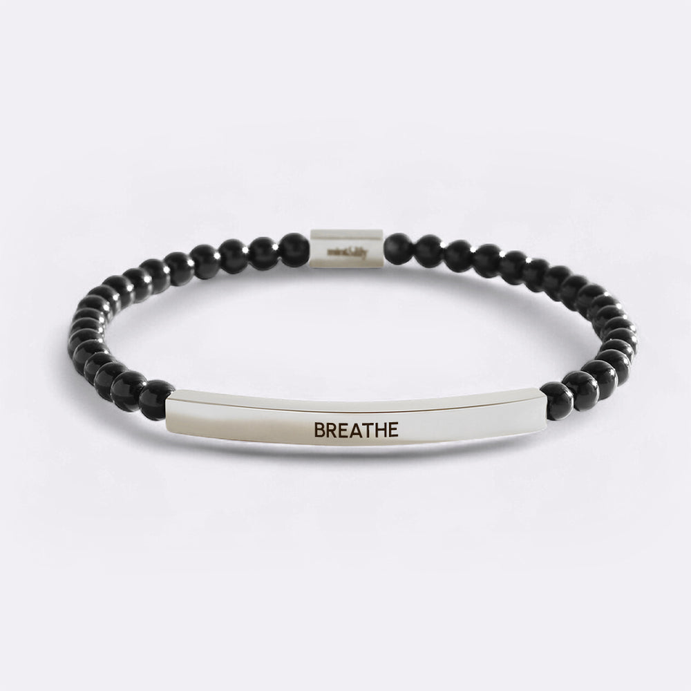 Black beaded bracelet with a silver bar featuring the word 'BREATHE' on a light gray background