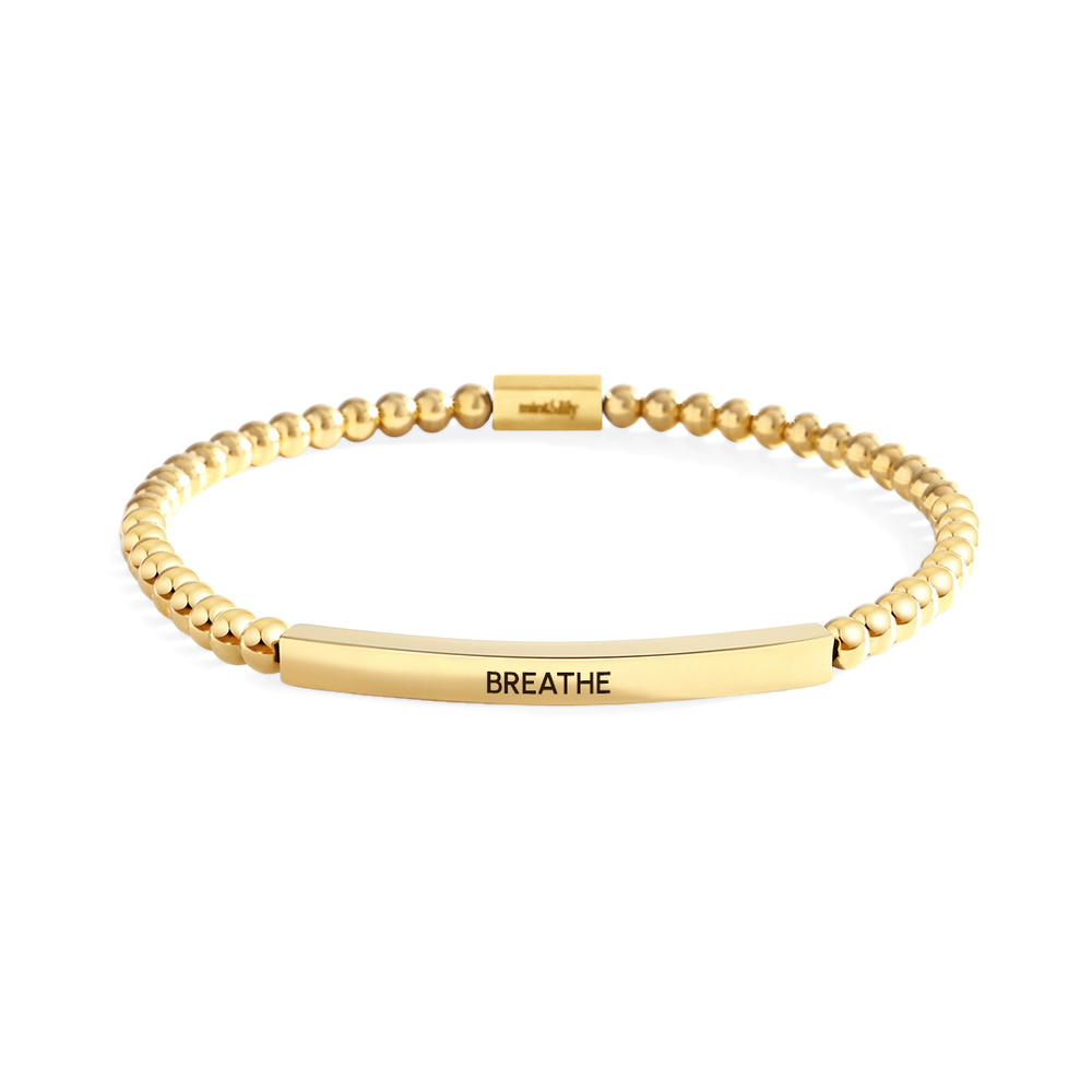 Gold bracelet with 'BREATHE' engraving on a light gray background