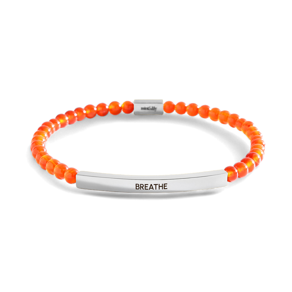 Orange beaded bracelet with silver bar and 'BREATHE' engraving on a light gray background