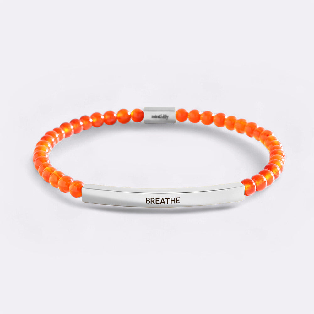 Orange beaded bracelet with silver bar and 'BREATHE' engraving on a light gray background