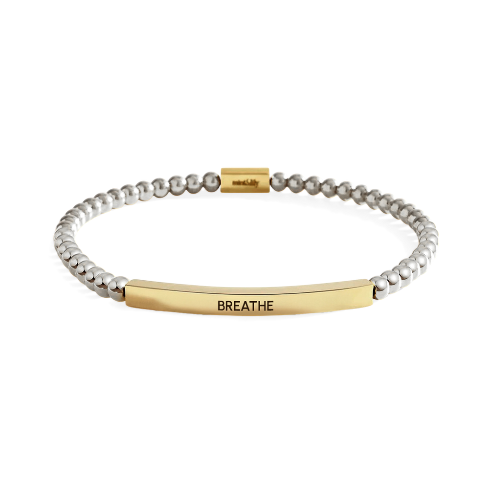 Bracelet with gold and silver beads and 'BREATHE' tag on a white background