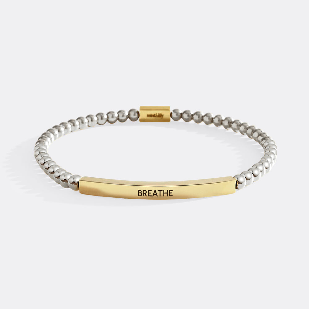 Bracelet with gold and silver beads and 'BREATHE' tag on a white background