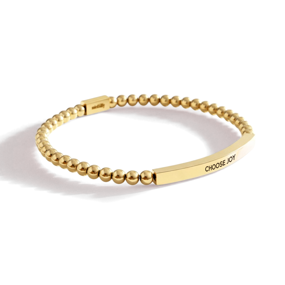 Gold beaded bracelet with a engraved tag on a light background