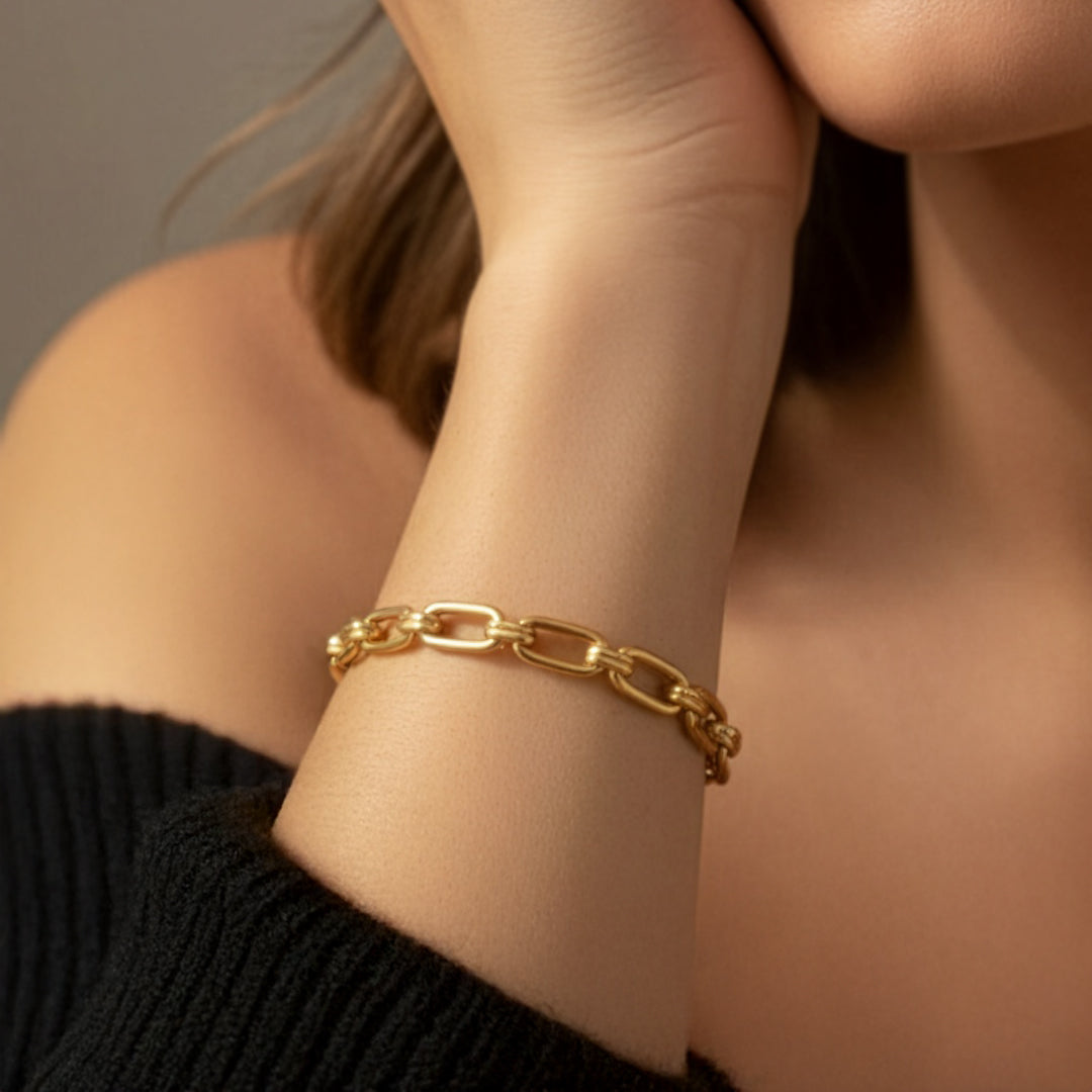 Gold chain bracelet on a person's wrist with a neutral background
