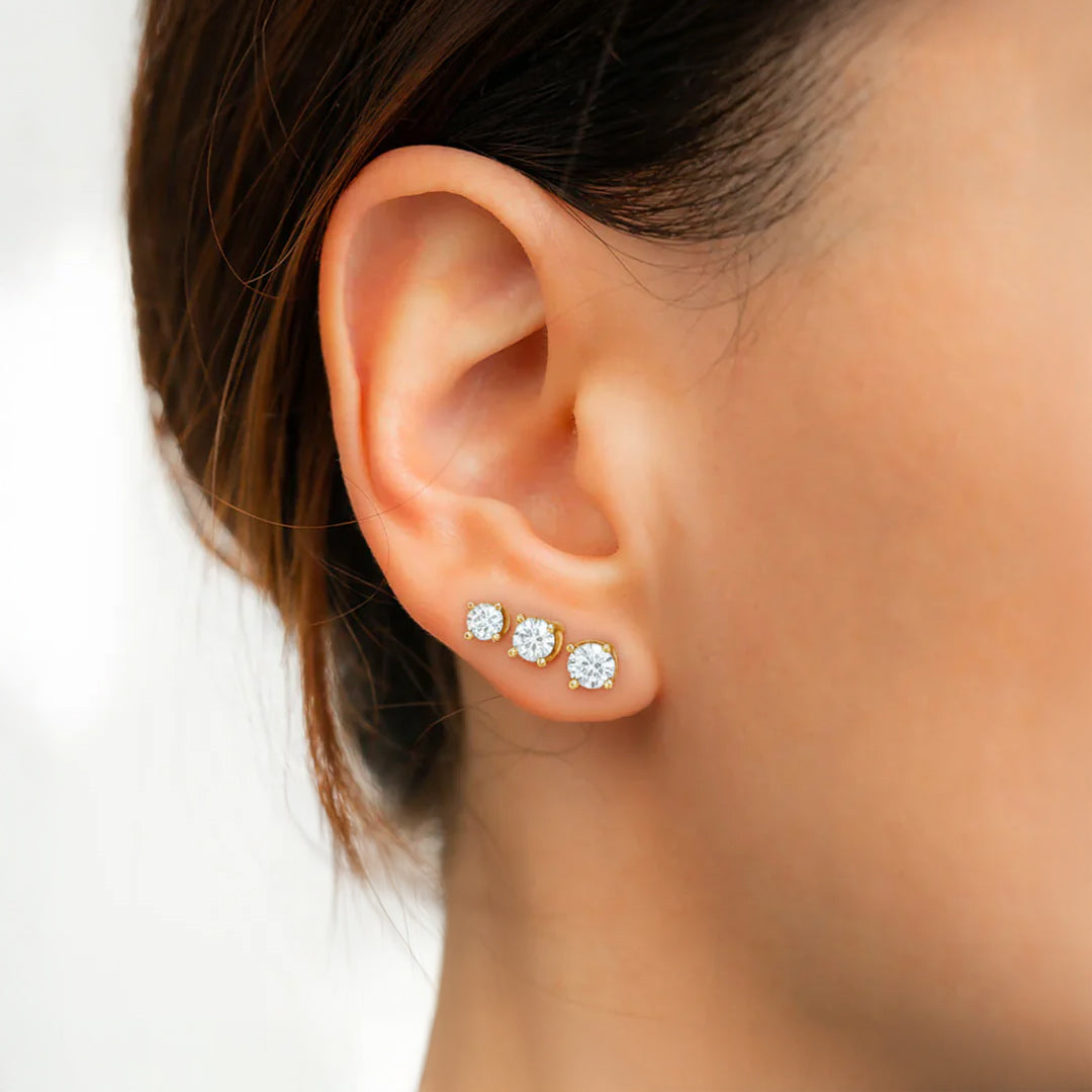 Close-up of an ear wearing three diamond stud earrings on a blurred background