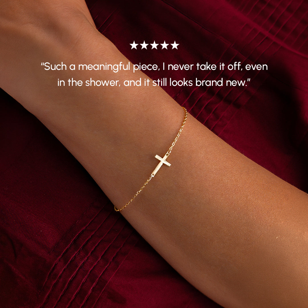 Gold bracelet with a cross on a wrist, against a red background.