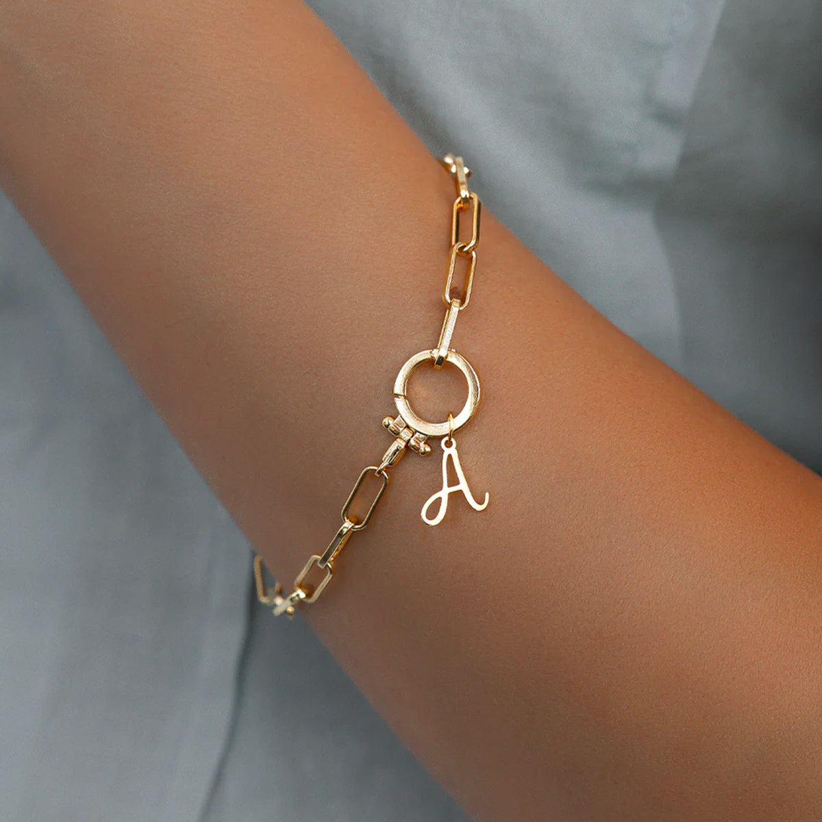 Gold bracelet with a letter 'A' charm on a wrist against a neutral background