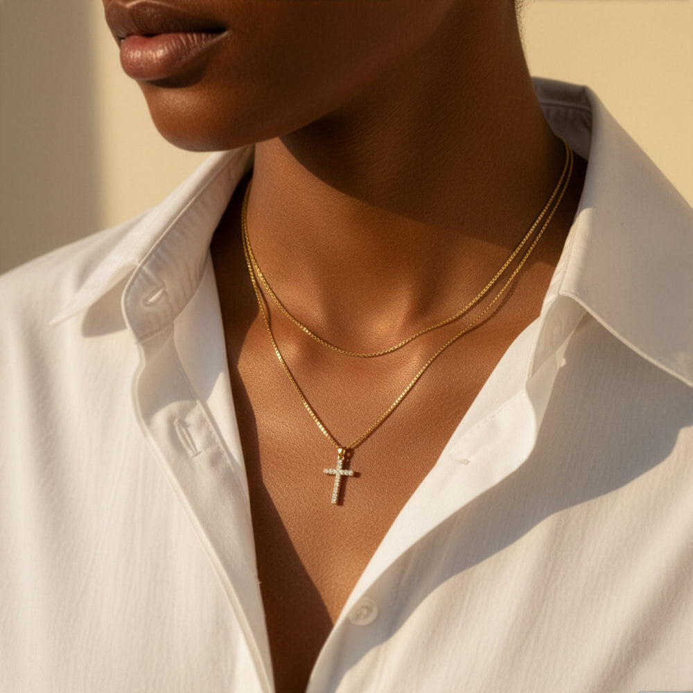 Close-up of a person wearing a gold necklace with a cross pendant, against a neutral background.