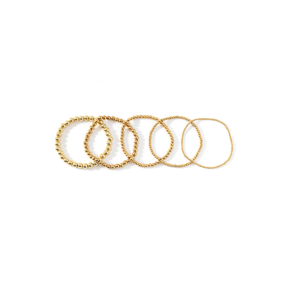 Dainty gold beaded bracelet flatlay of all five bead sizes on white background