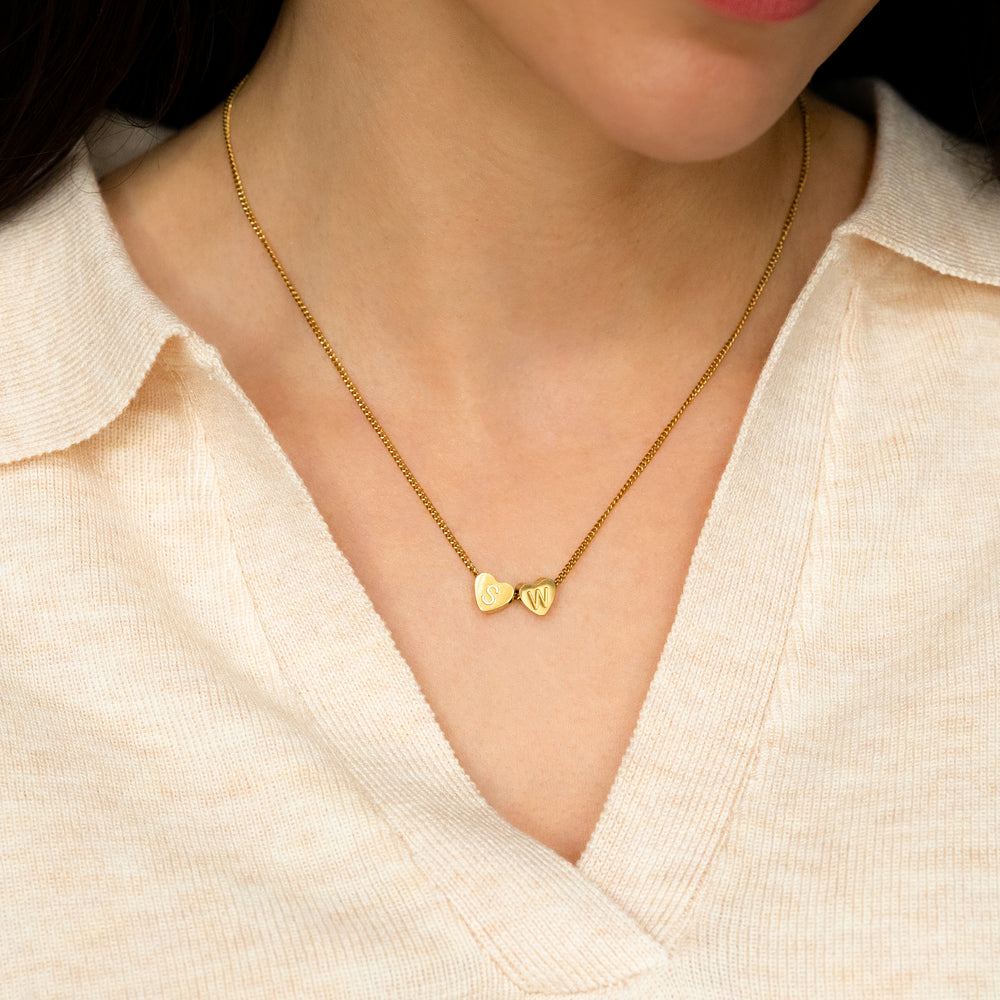 Gold necklace with heart pendants worn by a person in a light-colored top.