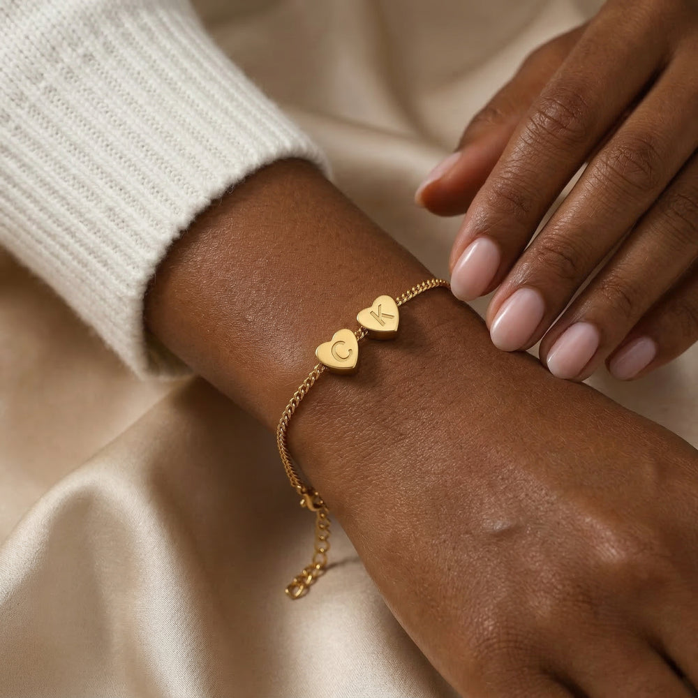 Gold bracelet with heart-shaped charms on a wrist against a beige background