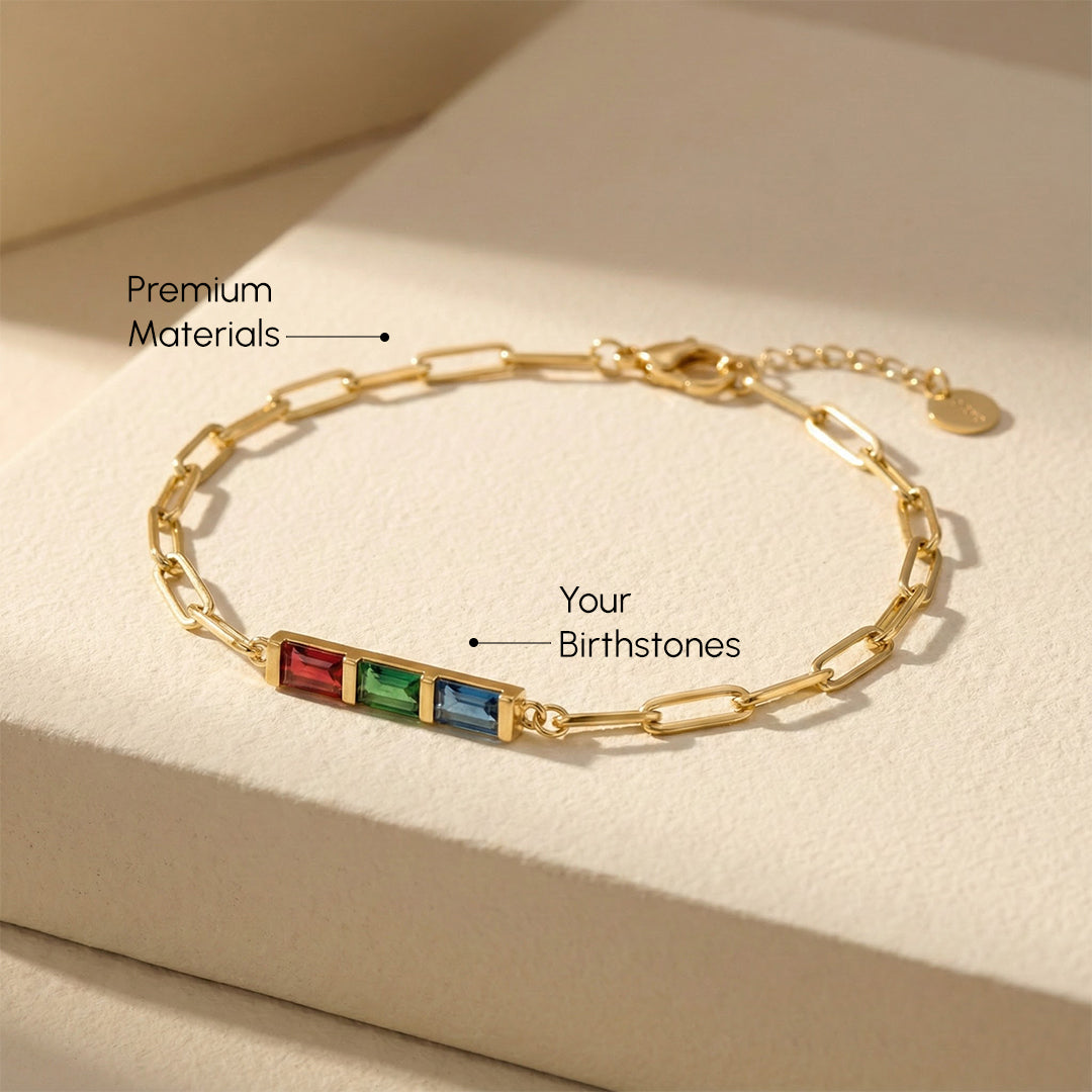 Gold bracelet with red, green, and blue stones on a beige surface