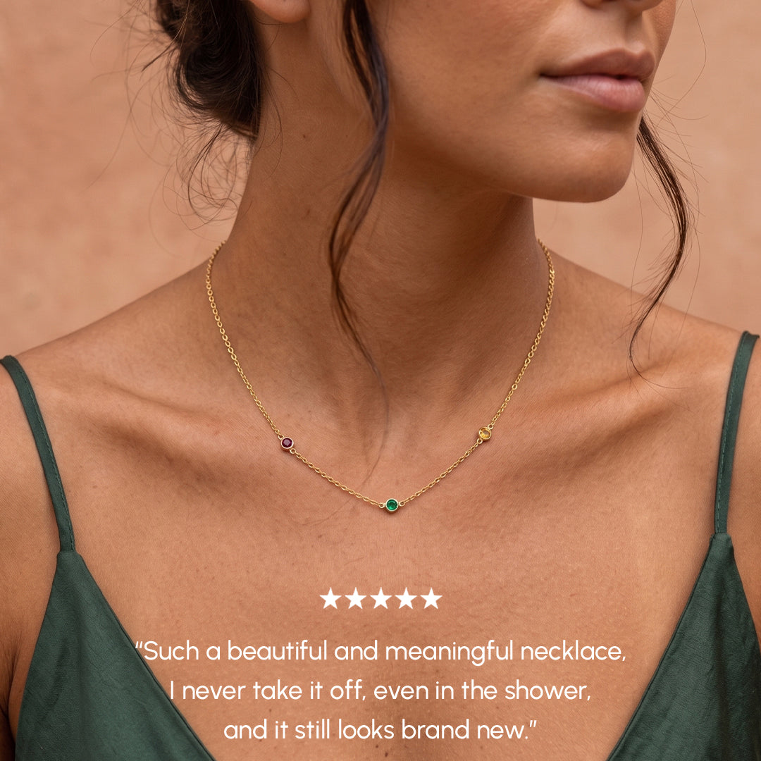 Woman wearing a gold necklace with green gemstone, against a neutral background.