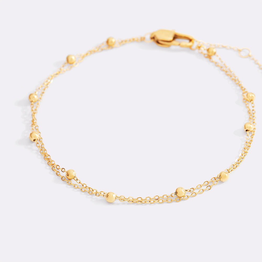Gold bracelet with small beads on a light gray background