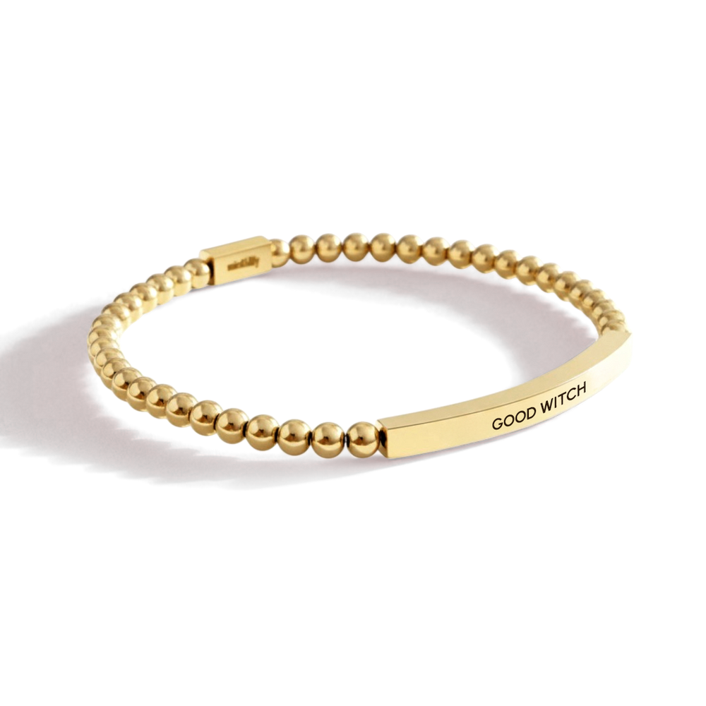 Gold beaded bracelet with 'GOOD WITCH' engraving on a white background