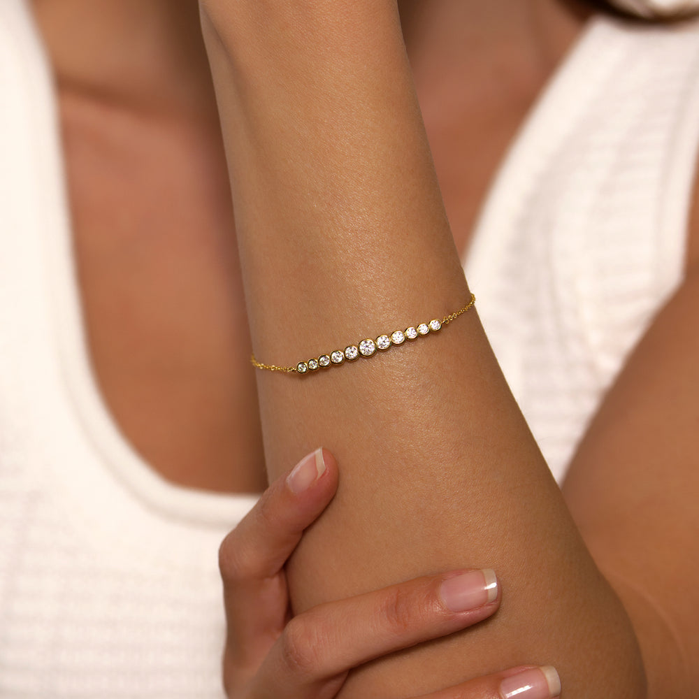 Gold bracelet with small diamonds on a wrist against a neutral background