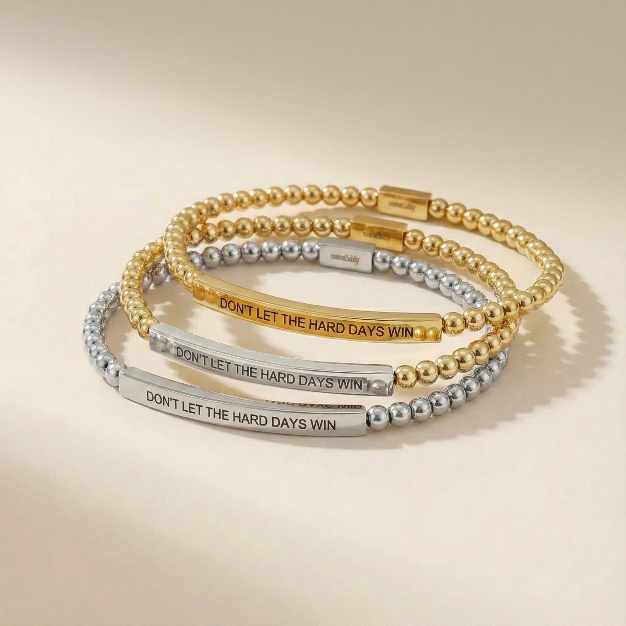 Three gold and silver beaded bracelets with motivational text on a beige background