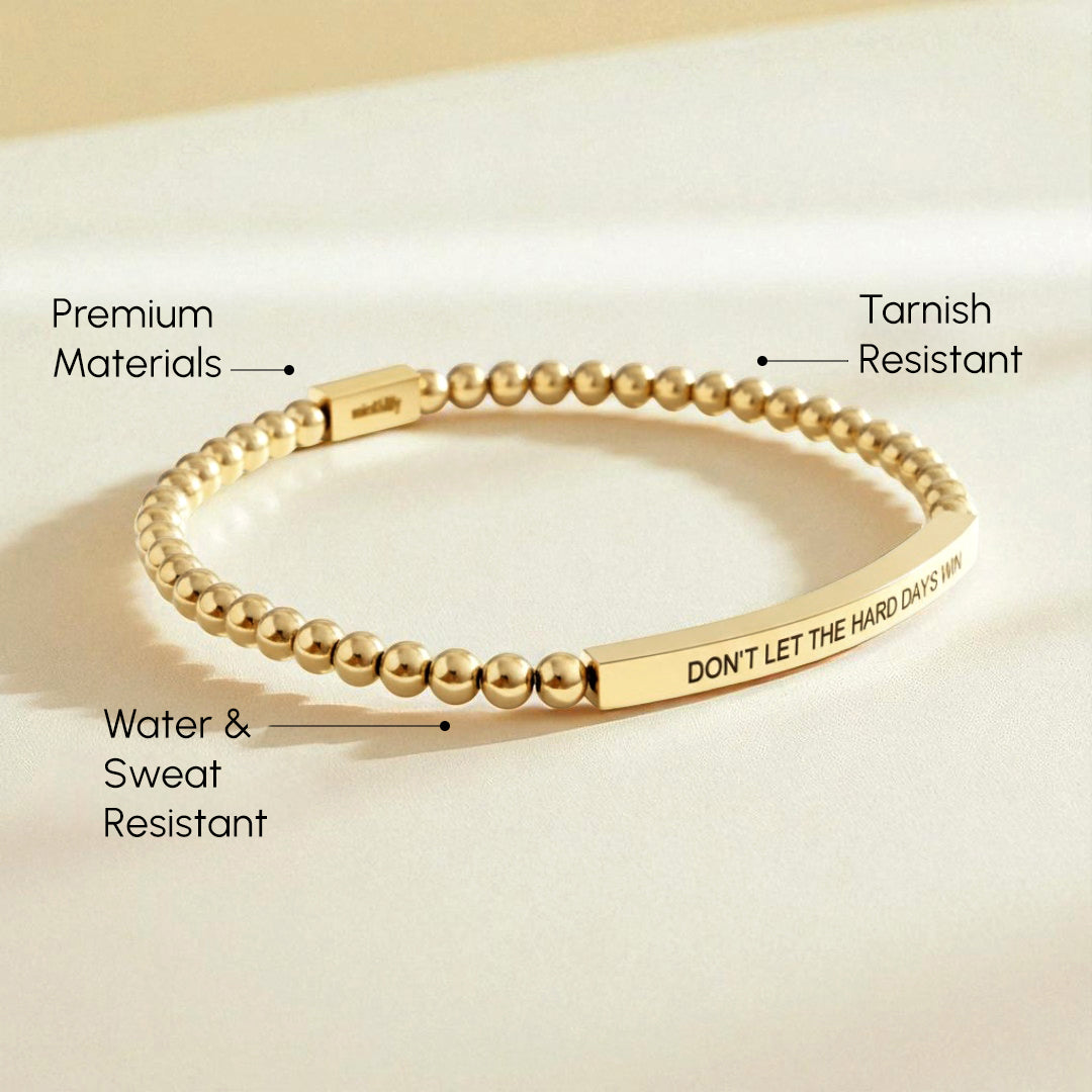 Gold beaded bracelet with engraved message on a beige background