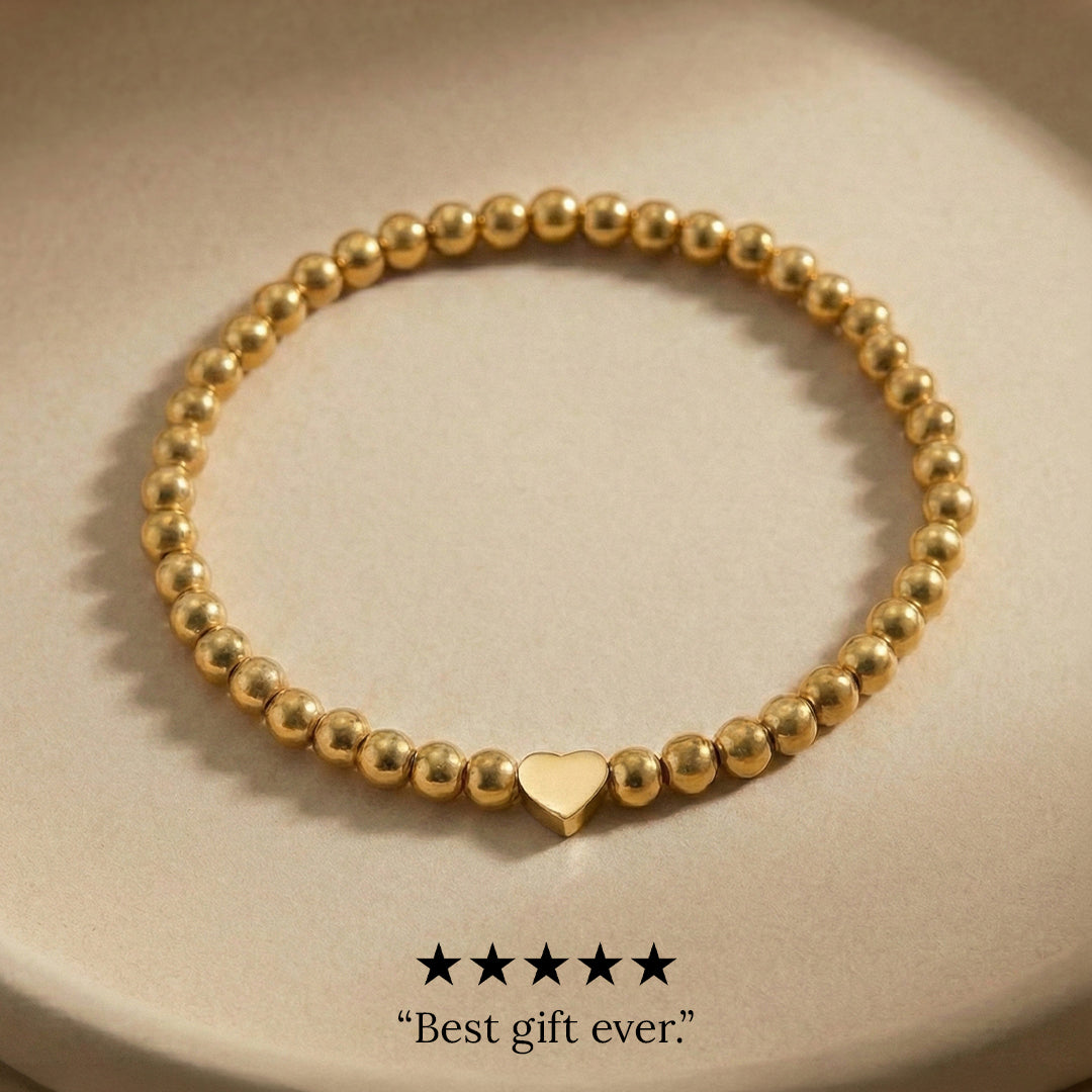 Gold beaded bracelet with a heart charm on a beige background