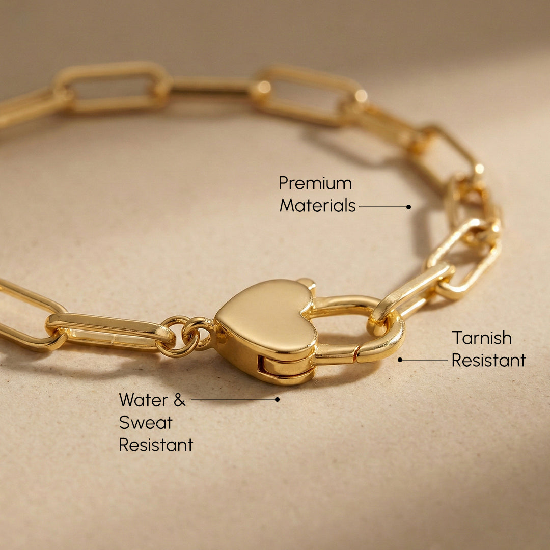 Gold bracelet with heart lock clasp on a beige background, labeled for material and resistance properties.