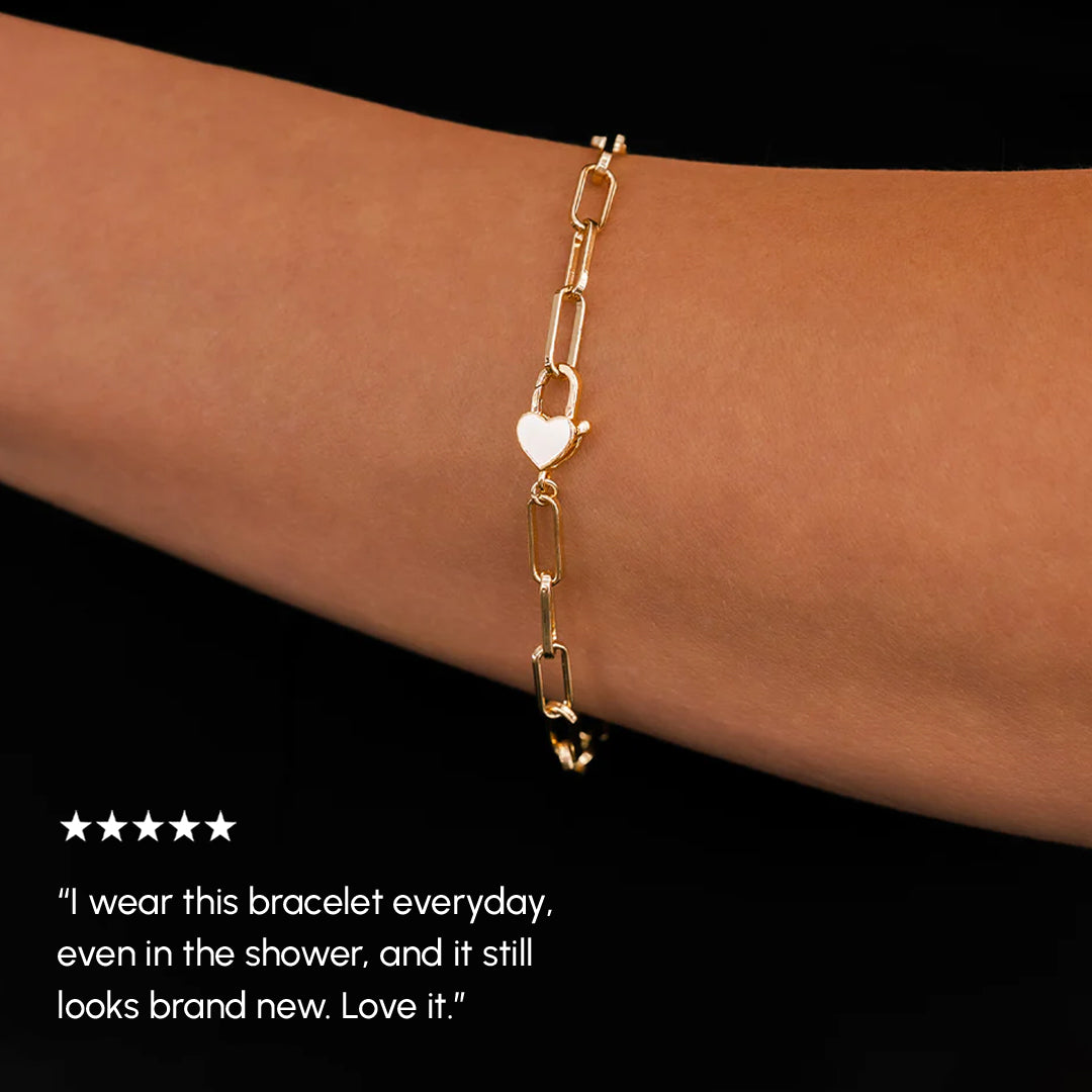 Gold bracelet with heart charm on a wrist against a black background