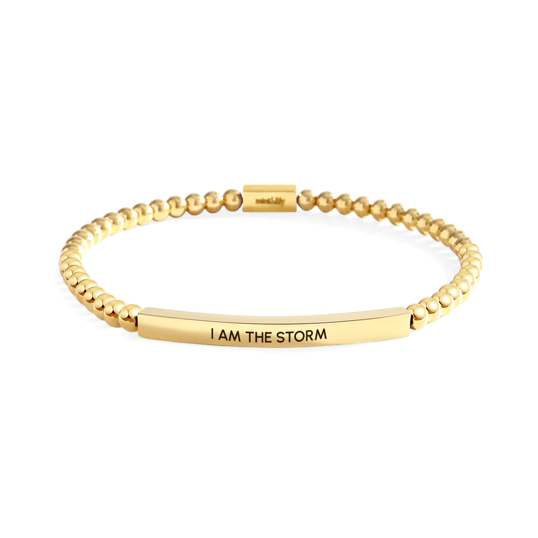 Gold bracelet with 'I AM THE STORM' engraving on a white background
