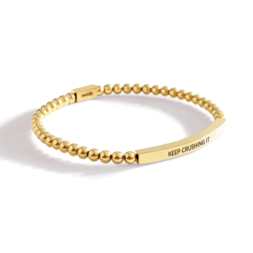 Gold beaded bracelet with a bar charm on a white background