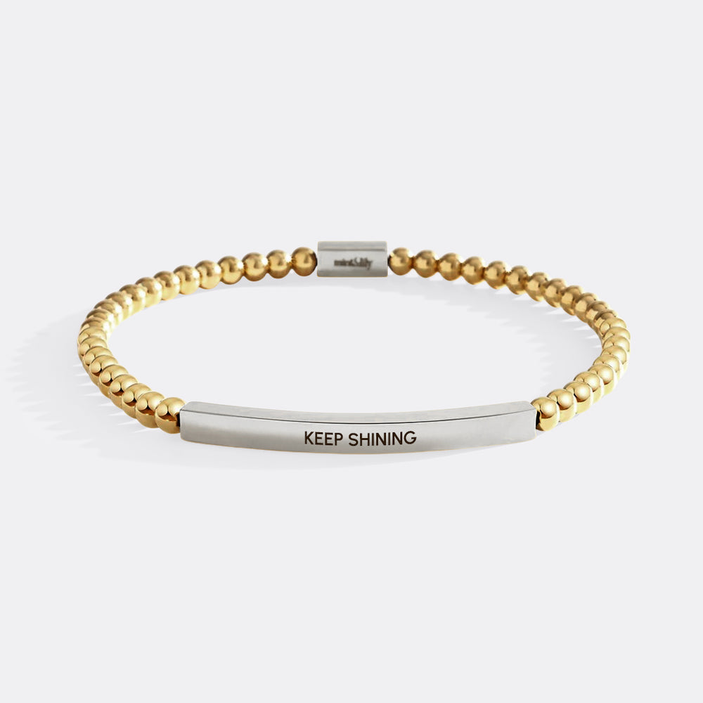 Gold beaded bracelet with silver bar and 'KEEP SHINING' engraving on a white background