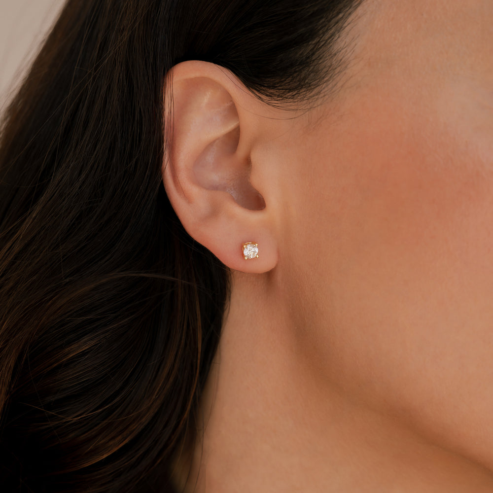 Close-up of an ear wearing a diamond stud earring with dark hair and skin background