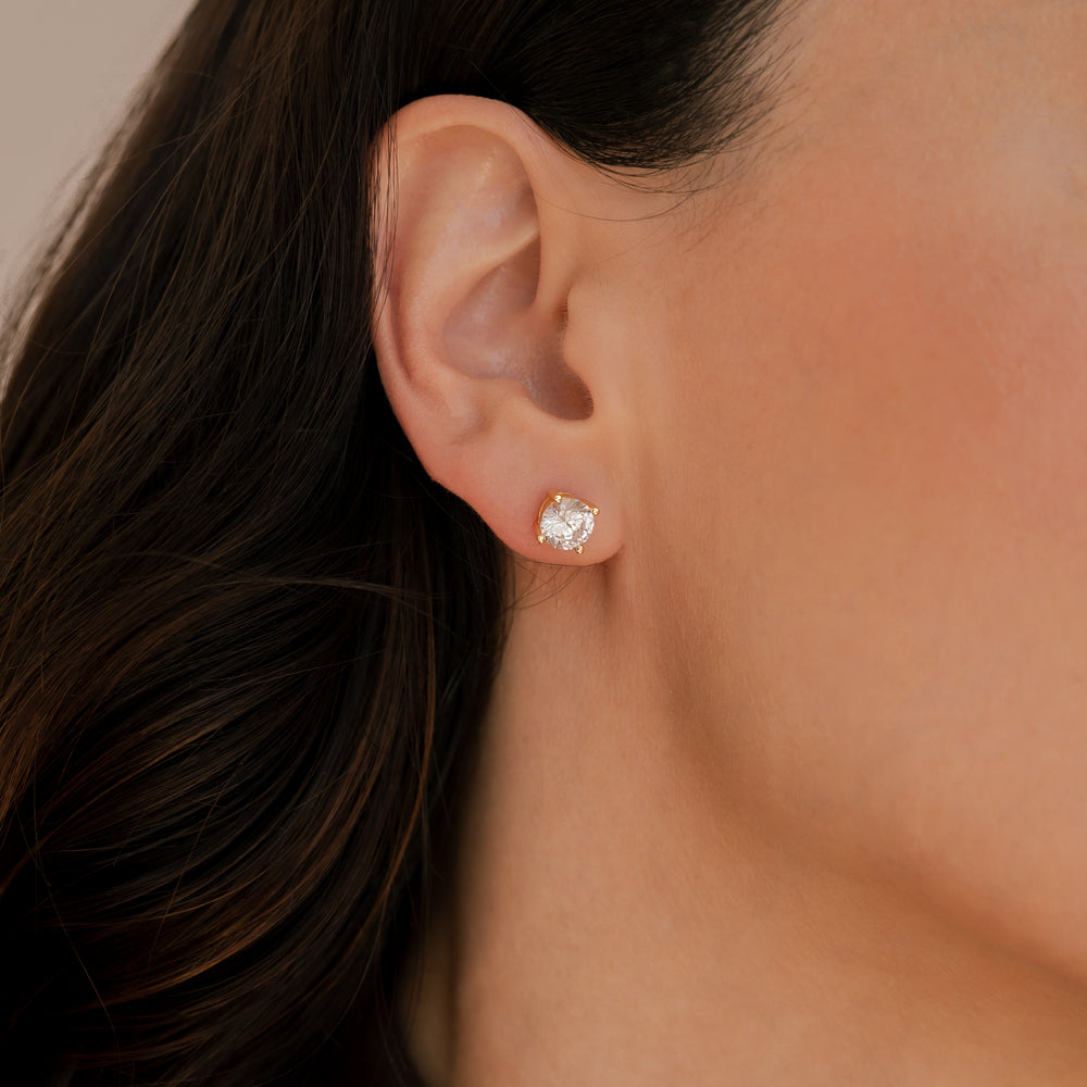 Close-up of an ear wearing a diamond earring with dark hair and skin in the background