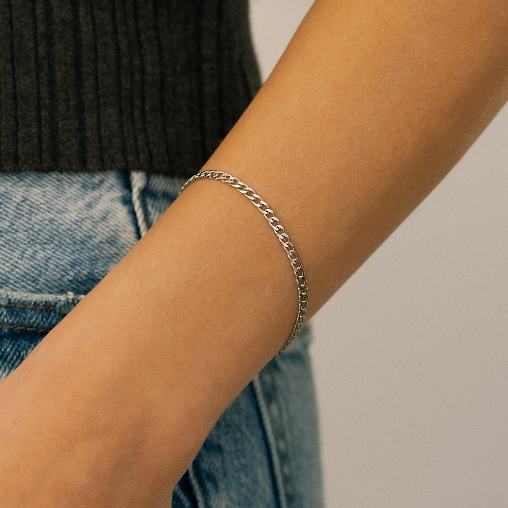 Silver chain bracelet on a person's wrist with a neutral background