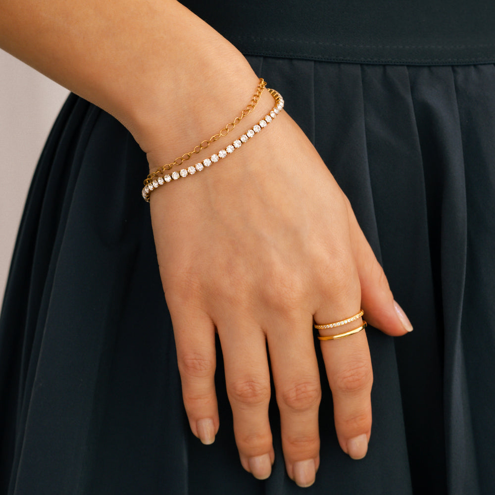 Hand wearing gold bracelets and a ring against a black background