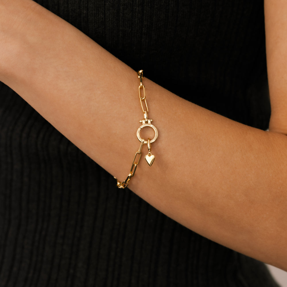 Gold bracelet with heart charm on a person's wrist against a black background